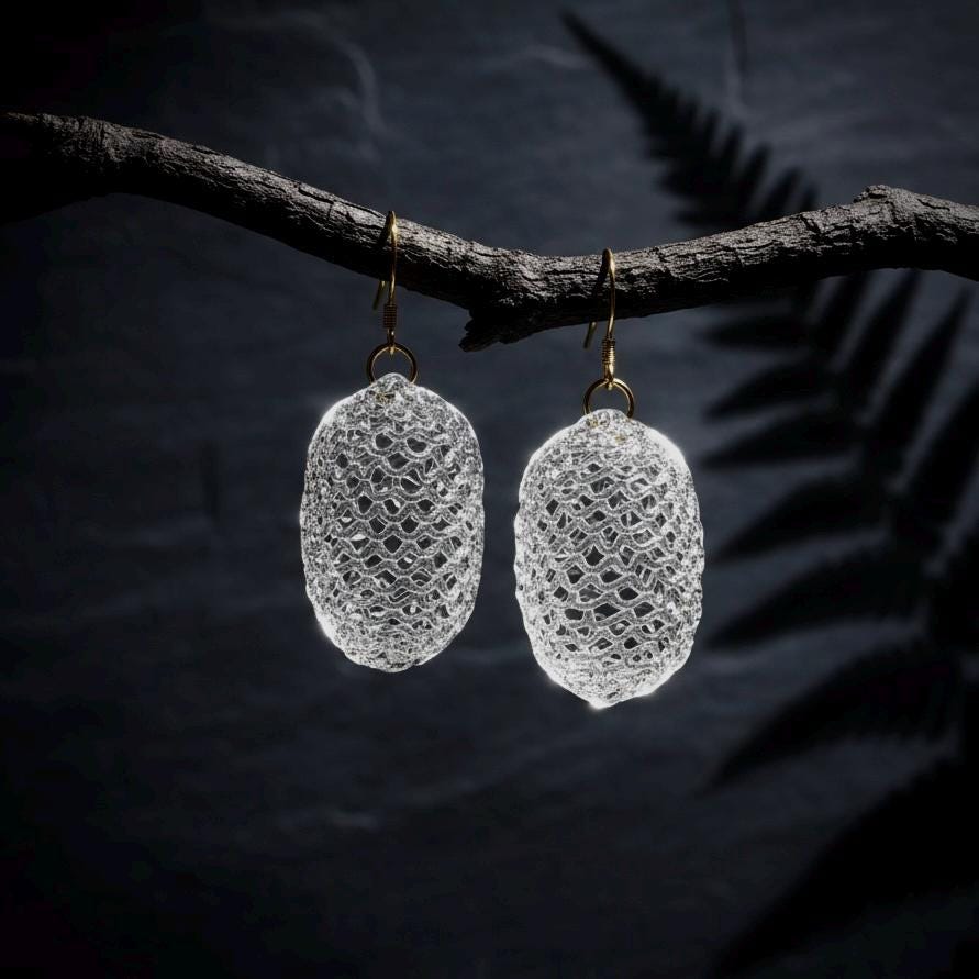 Woven glass cocoon earrings suspended from a natural branch